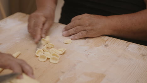 imágenes en cámara lenta de una anciana cortando y enrollando masa de pasta en conchas de conchiglie en bari, italia