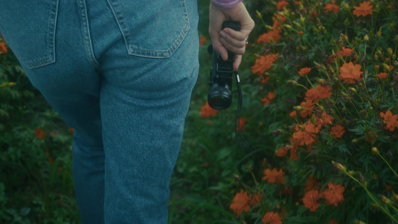 Mujer caminando por un jardín de flores sosteniendo una cámara vintage