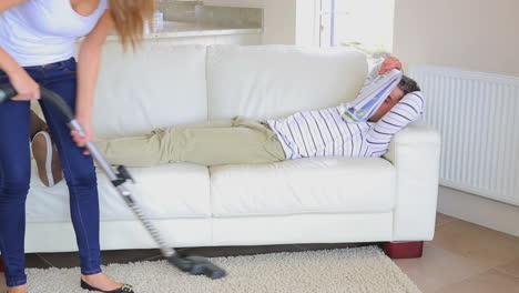 woman cleaning the room while man reading newspaper