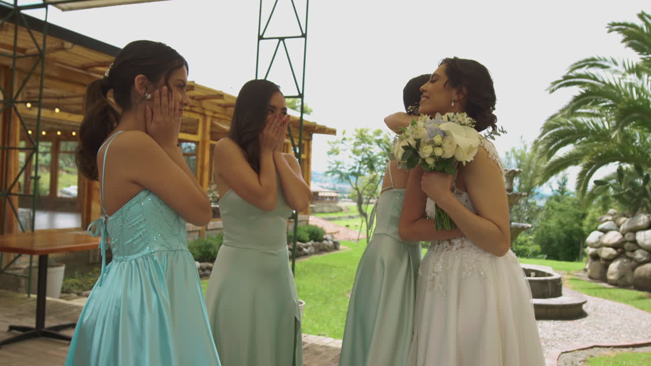 A touching moment in which the bridesmaids happily run toward the bride and hug her joyfully. The bride holds her bouquet while everyone shares a moment filled with affection and emotion.