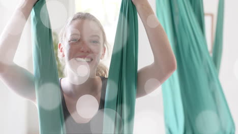 Animation-of-light-spots-over-happy-caucasian-teenage-girl-practicing-aerial-yoga