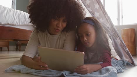 video de una feliz madre y hija afroamericanas acostadas en una tienda de campaña y usando una tableta juntas