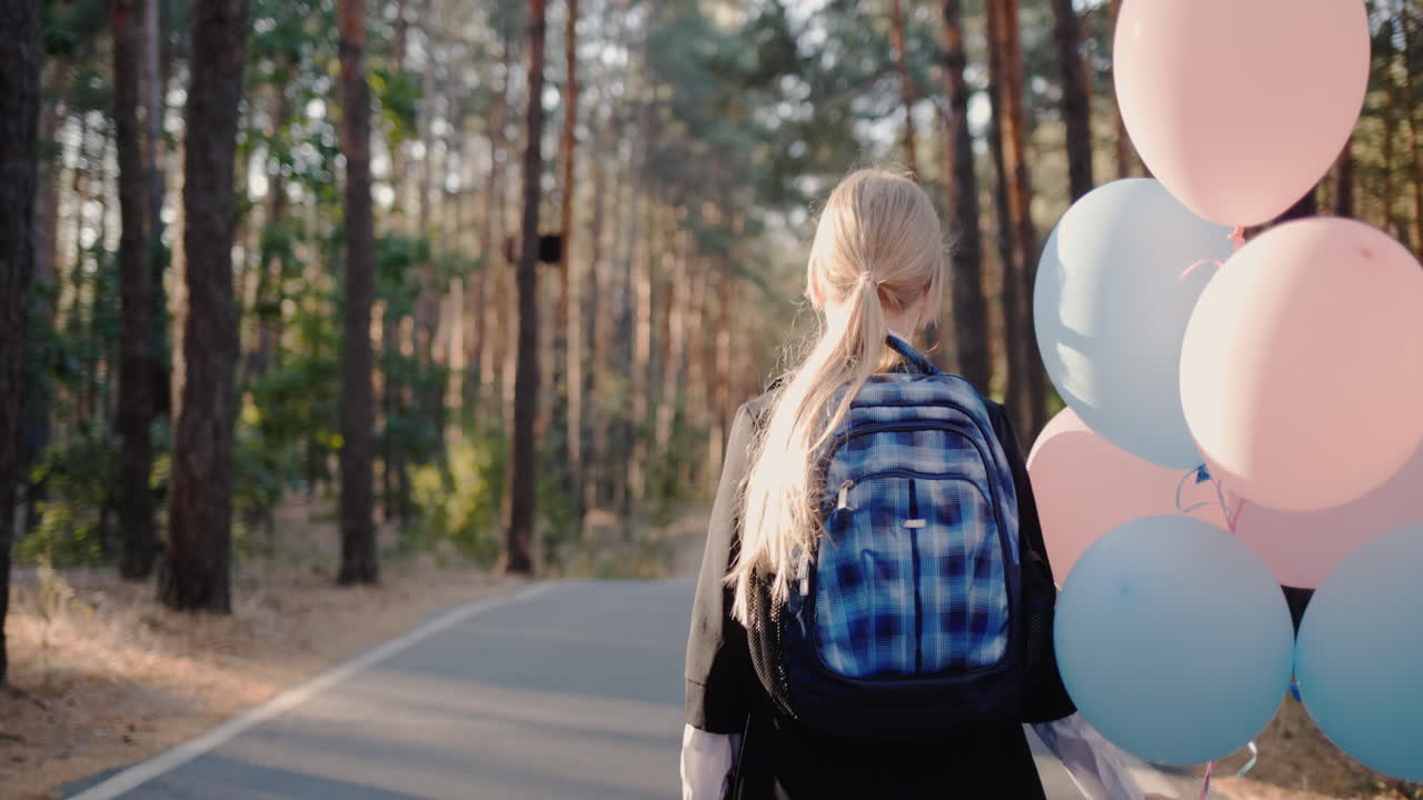 백팩과 풍선을 든 여학생이 공원 길을 걷는다