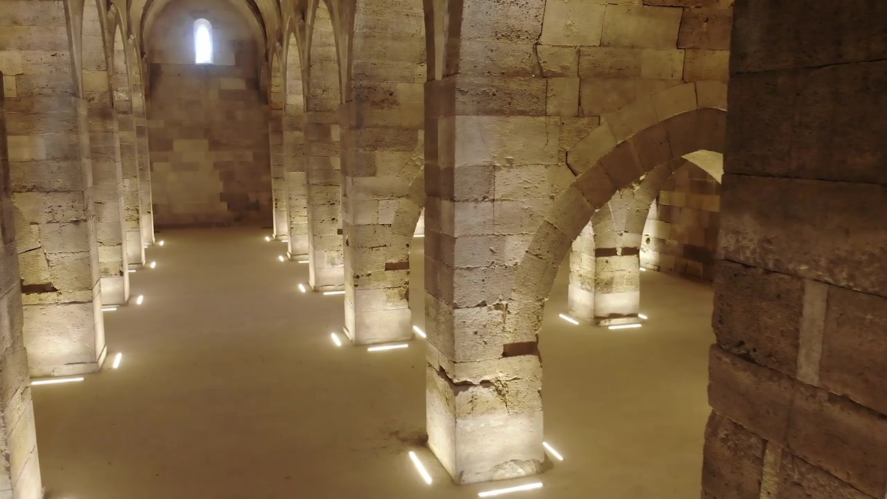 Pessoa Caminhando por um Antigo Salão Abobadado de Pedra com Iluminação Ambiente