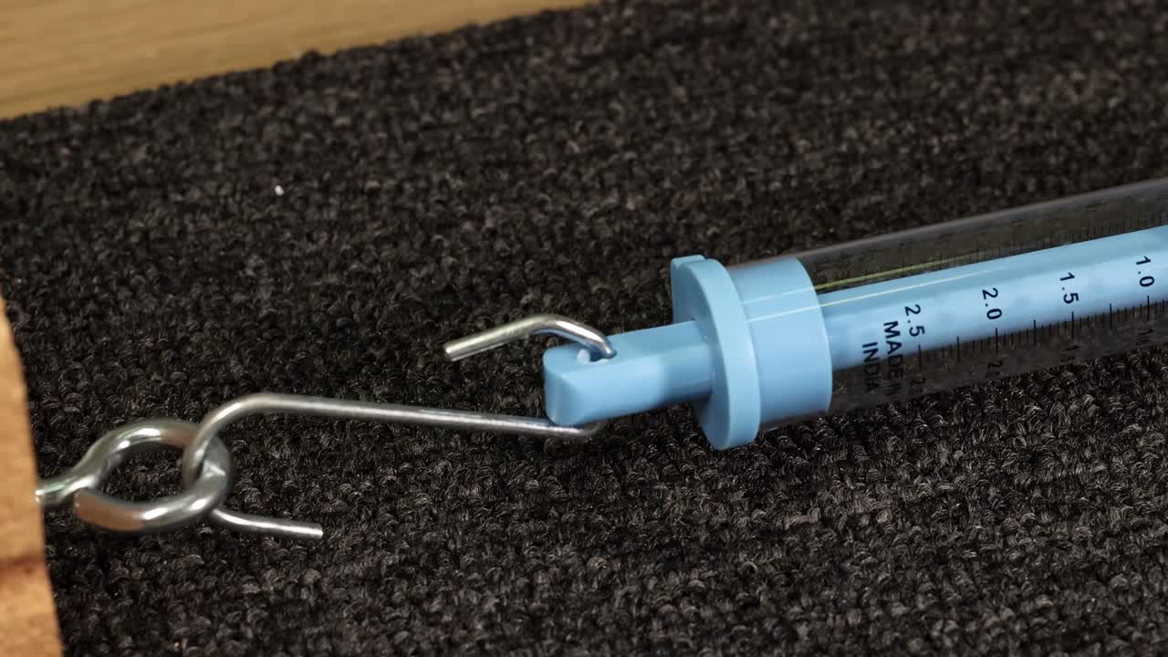 A hand uses a spring scale to measure friction between a wooden block and surface. Close-up, macro view with natural lighting