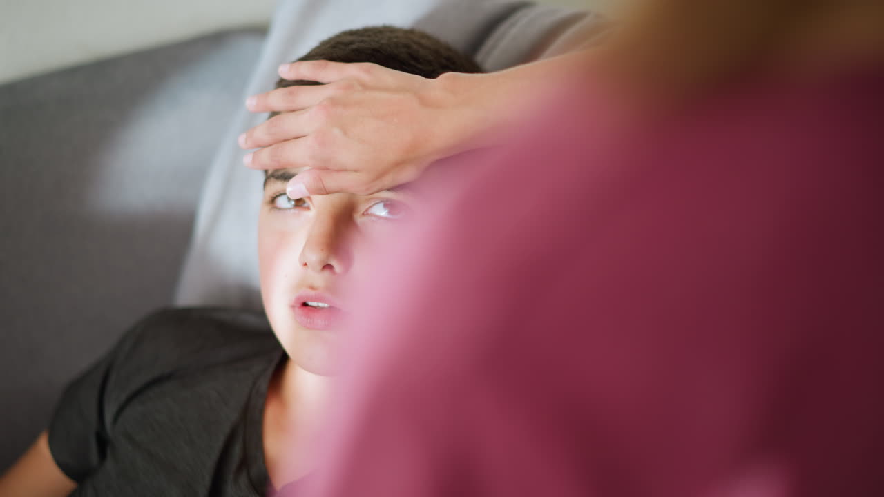 Close-up of rear view of caregiver checking on sick child laying down with eyes closed, child slowly opens eyes and looks at the person, a caring moment in a comforting home environment