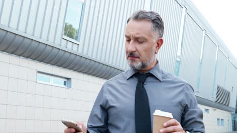 close-up view of gray-haired businessman holding coffee cup and using smartphone in the street