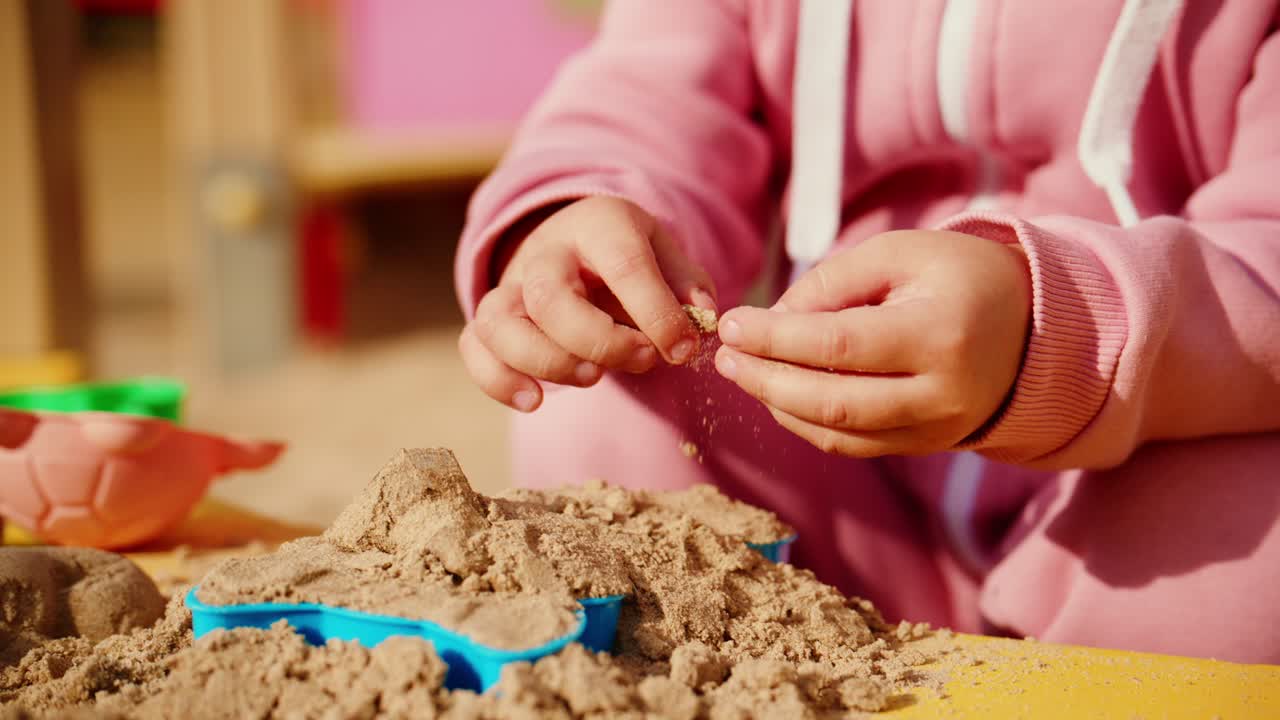 Kind spielt im Sand, formt und kreiert begeistert Formen mit den Händen in einem farbenfrohen Spielbereich, lebt Fantasie und fröhliche Outdoor-Aktivitäten aus