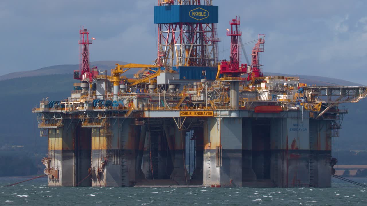 Stor offshore olieplatform flyder på oprørt hav, fjerne bakker, dagslys, stabilt kamera
