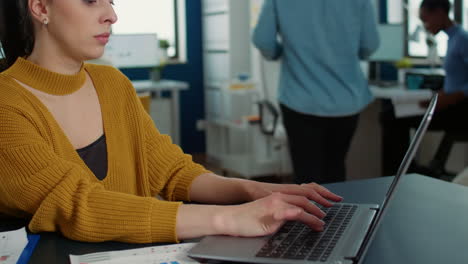 Portrait-of-woman-typing-using-laptop-keyboard-and-smiling-at-camera-sitting-at-desk