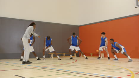 basketball coach training high school team in gym, players practicing defense