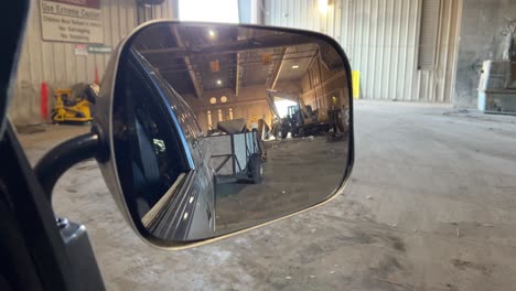 looking through a mirror of a truck as it backs up a trailer full of junk at the dump you can also see some large industrial vehicles in the background