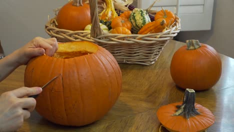 mujer cortando el ojo derecho de una calabaza en una mesa de comedor con luz natural desde un lado