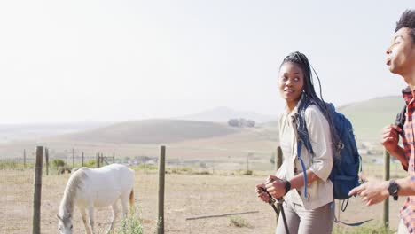 Happy-african-american-couple-with-backpacks,-hiking-with-trekking-poles-together,-slow-motion