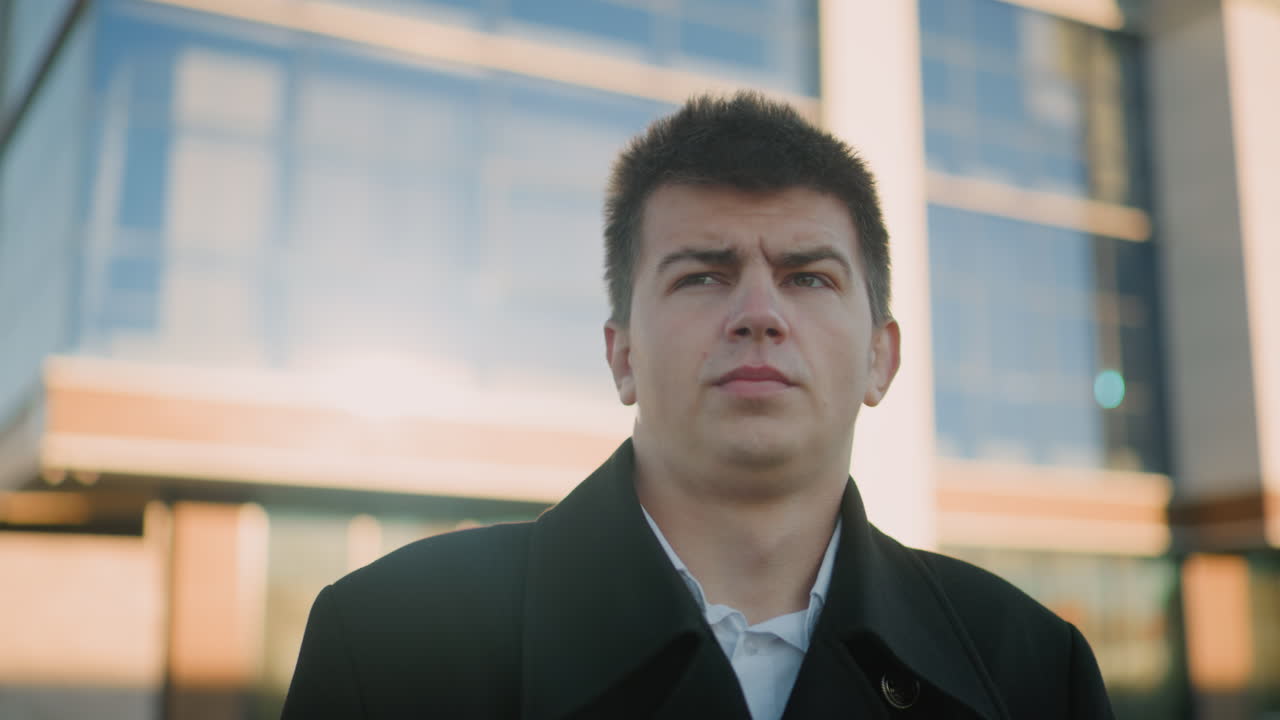 검은 옷을 입은 남자가 집중적이고 진지한 표정으로 목걸이를 조정합니다. 빛은 그의 특징을 강조합니다. 유리 건물 배경에 서서 결단력을 묘사합니다.