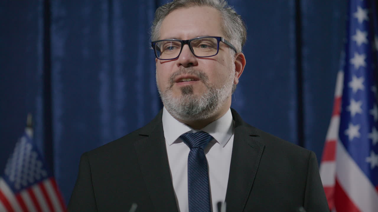 Political Leader Speaking to Press at Podium with American Flags Behind