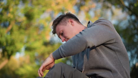 close up of young man in gray hoodie focused intently as he holds black and orange strap, appearing deep in thought or concentration, against a blurred natural outdoor background