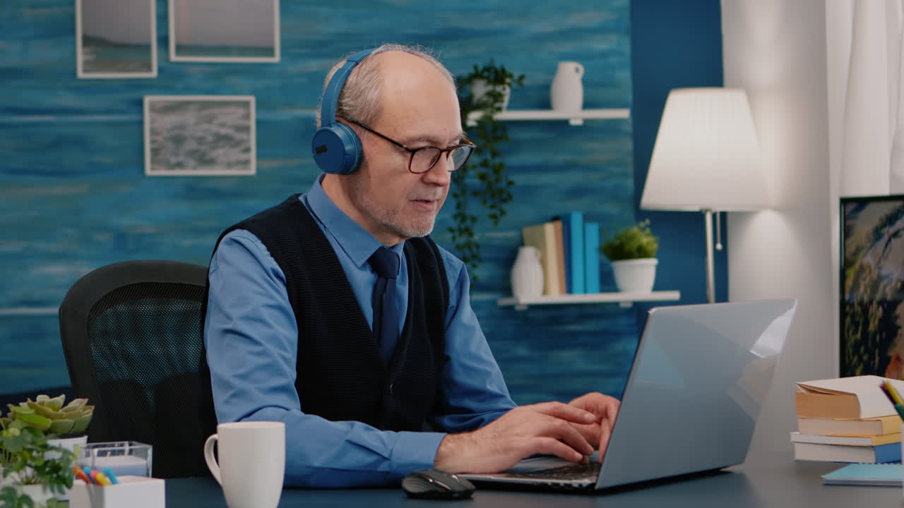 Focused old entrepreneur with headphones listening music typing on laptop