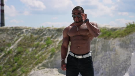 portrait of muscular black skinned man outdoors. african american sportsman without shirt wearing black sunglasses shows his trained body on camera.