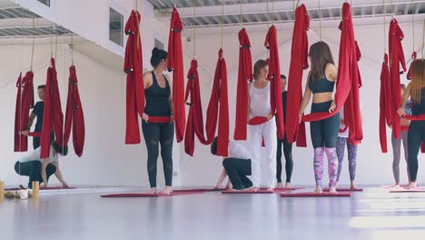 women-group-prepares-for-fly-yoga-workout-with-red-hammocks