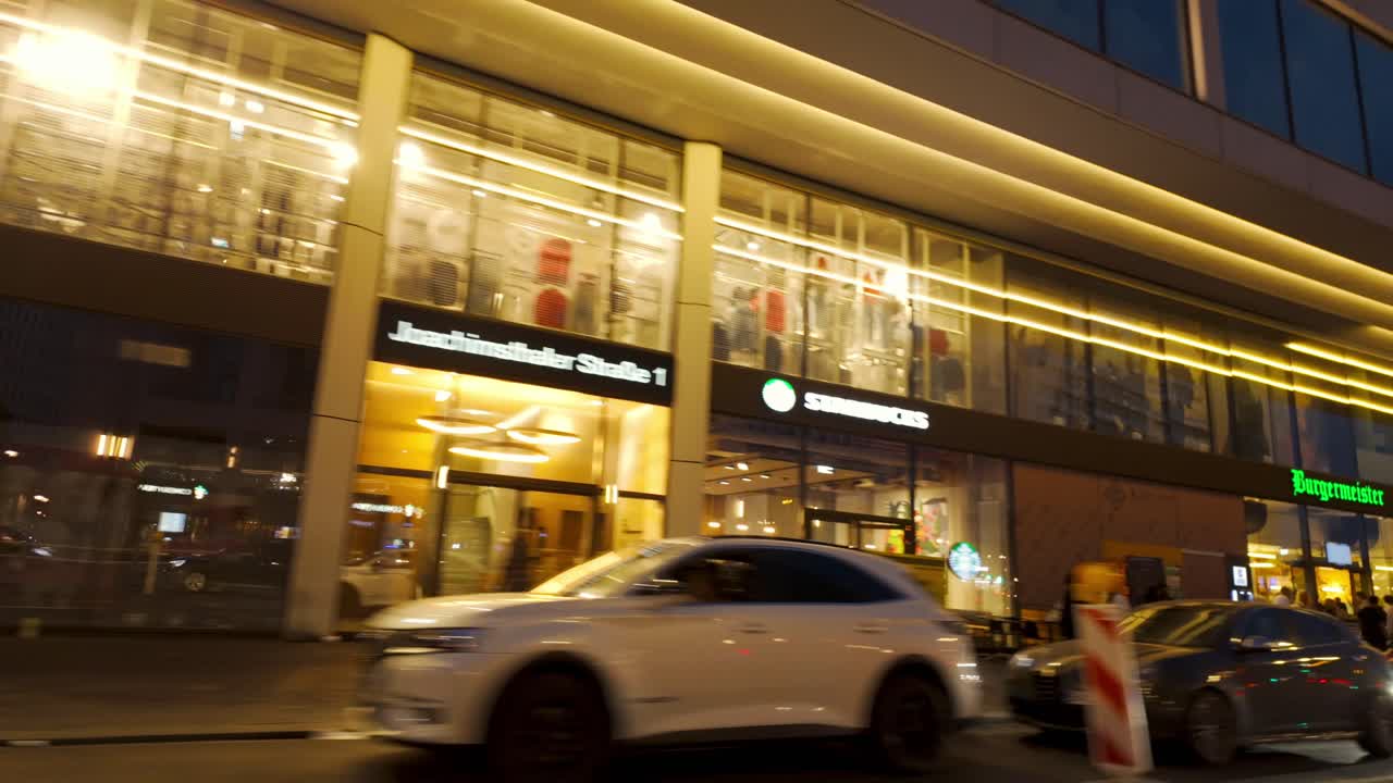 Night street view in Berlin, captured from inside a car. Illuminated modern building, busy pedestrians, and vibrant city life. Urban nightscapes and city exploration
