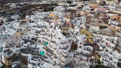 oia village cliffside houses and hotels in santorini, greece, cinematic aerial view