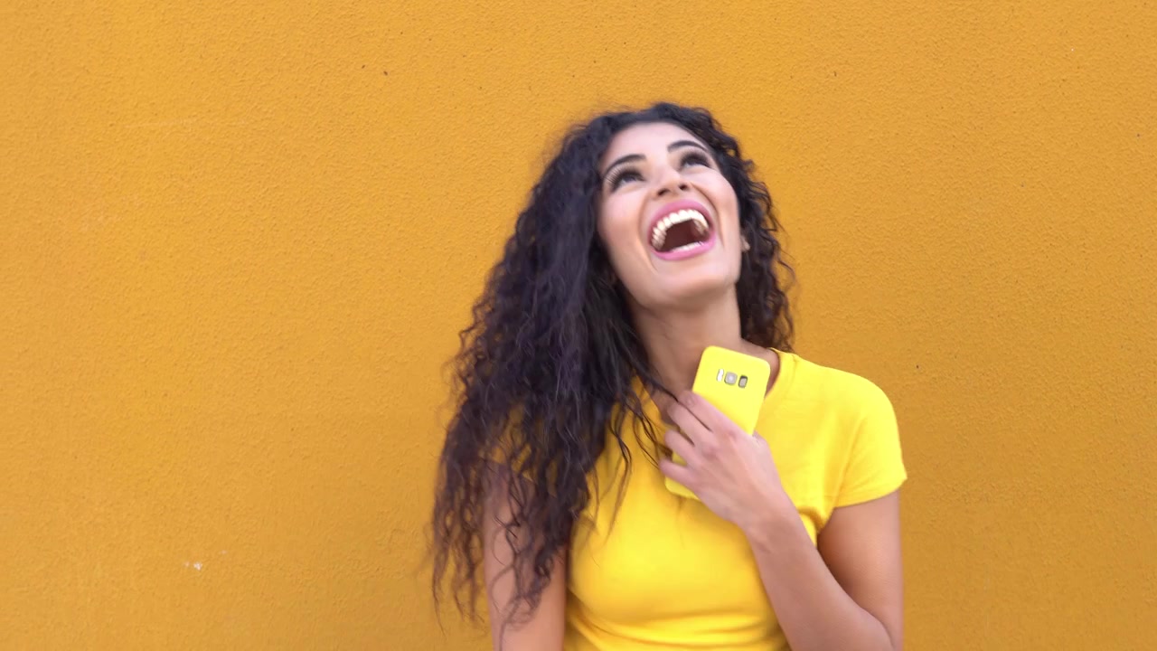 Giovane donna araba su un muro giallo per strada che sorride e ride