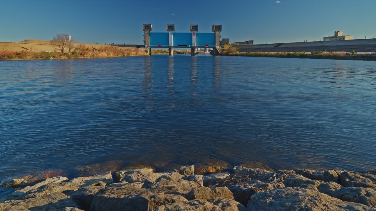 Un'inquadratura ampia della moderna chiusa blu Iwabuchi sul fiume Arakawa. L'acqua limpida e blu riflette la massiccia struttura di controllo delle inondazioni a Tokyo.