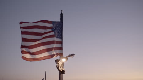 Handheld-slow-motion-shot-of-the-American-flag-shot-at-dusk-with-beautiful-purple,-orange-and-pink-hues-in-the-sky