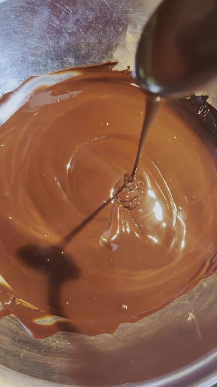 Primo piano di cioccolato al latte completamente fuso mescolato delicatamente con un cucchiaio, creando una consistenza liscia e lucida durante la preparazione di dolci e prodotti da forno