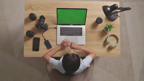 top view of asian woman video editor yawning and sleeping while using green screen laptop and smartphone next to the camera in the workspace at home