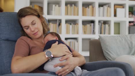 video de una madre caucásica cansada durmiendo en un sillón con un bebé recién nacido