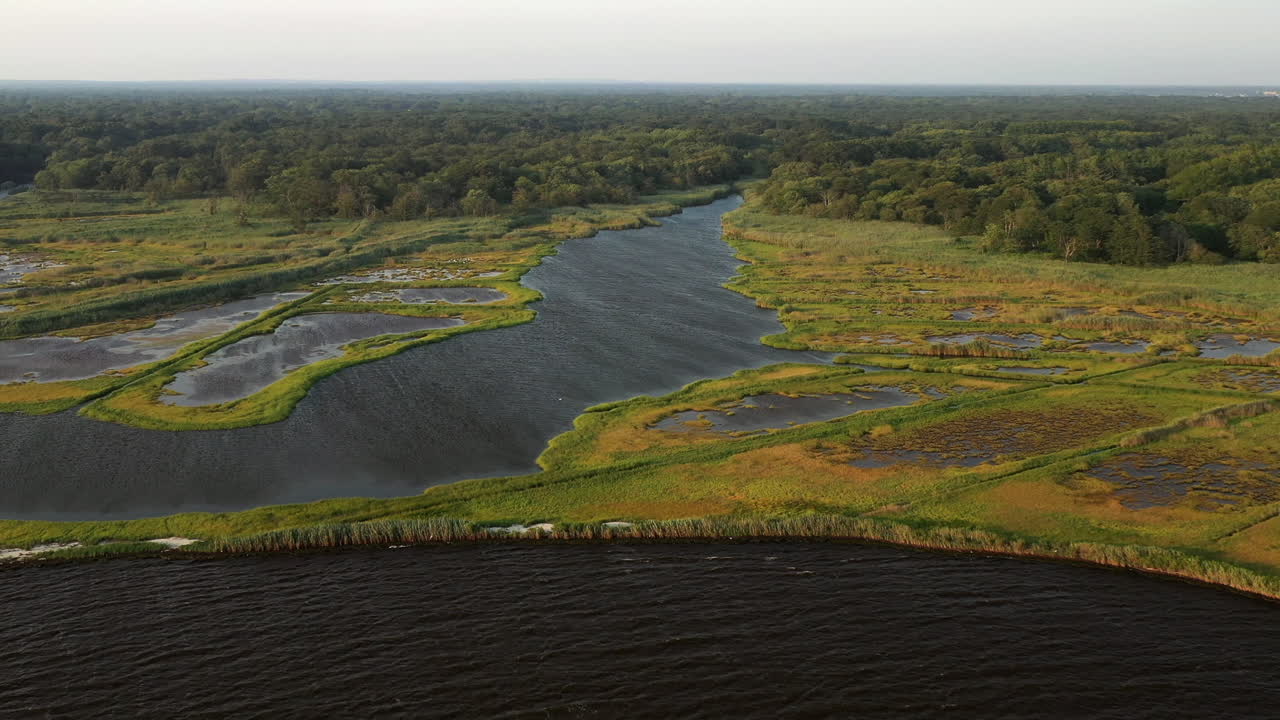 Ripresa aerea discendente sopra le acque del Parco Marina di East Islip, con focus sull'area della palude e un canale navigabile più ampio sulla sinistra, al tramonto.
