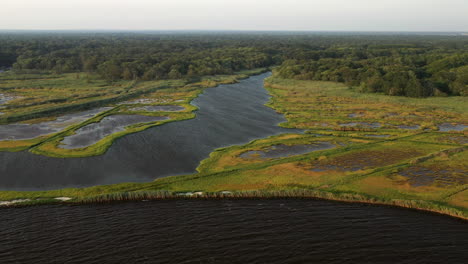 Absteigender-Kran-über-Den-Gewässern-Des-Jachthafens-East-Islip-Geschossen---Park-Mit-Schwerpunkt-Auf-Dem-Sumpfgebiet-Mit-Einem-Breiteren-Kanalwasserweg-Auf-Der-Linken-Seite-Bei-Sonnenuntergang