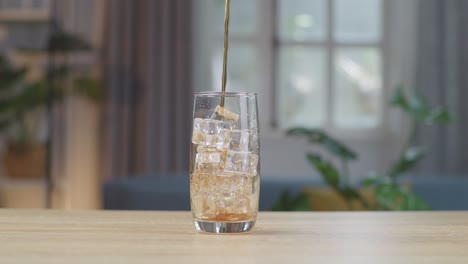 fresh cola being poured in to the glass with ice cubes on table