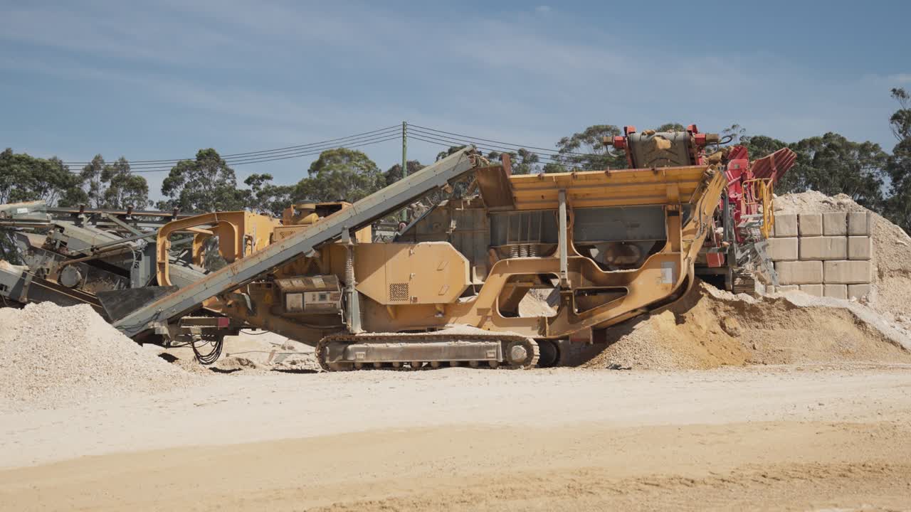 A mobile sand crusher processes raw material at a quarry site. The tracked machine crushes and screens sand for use in construction and cement production