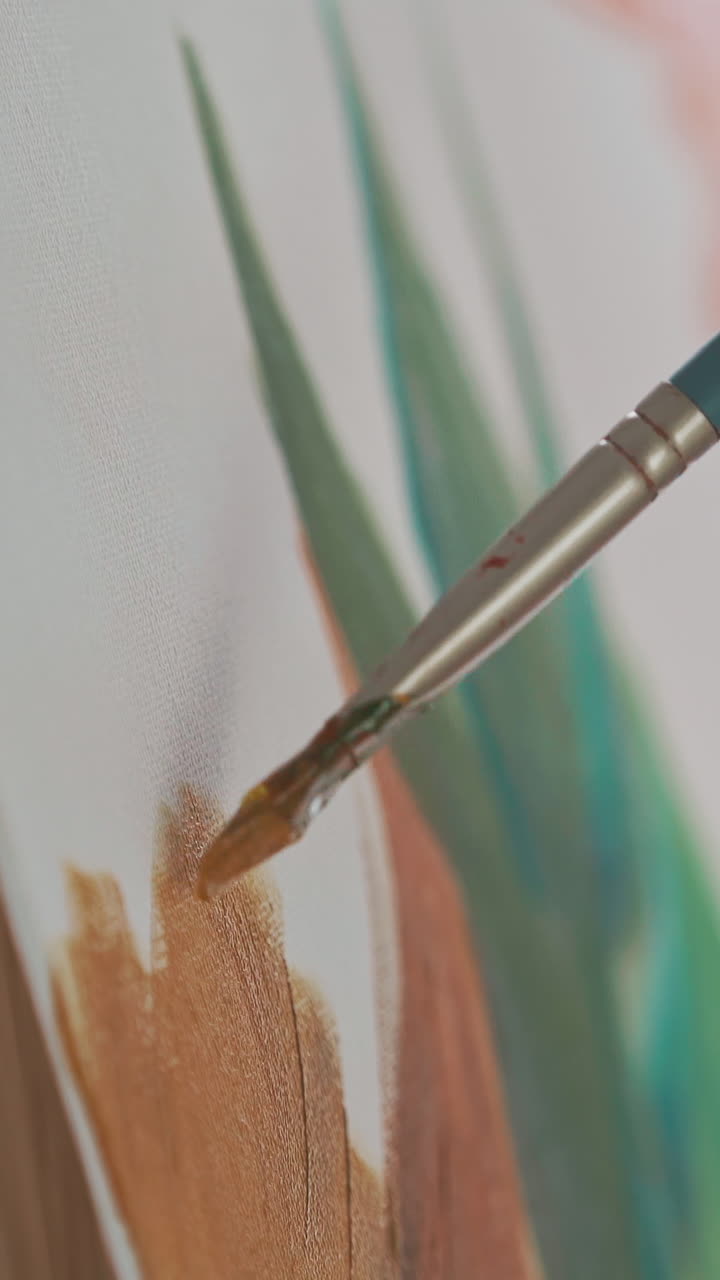 Young woman hand draws lush tropical plant with orange color on white canvas fixed on wooden easel in light art studio extreme close view