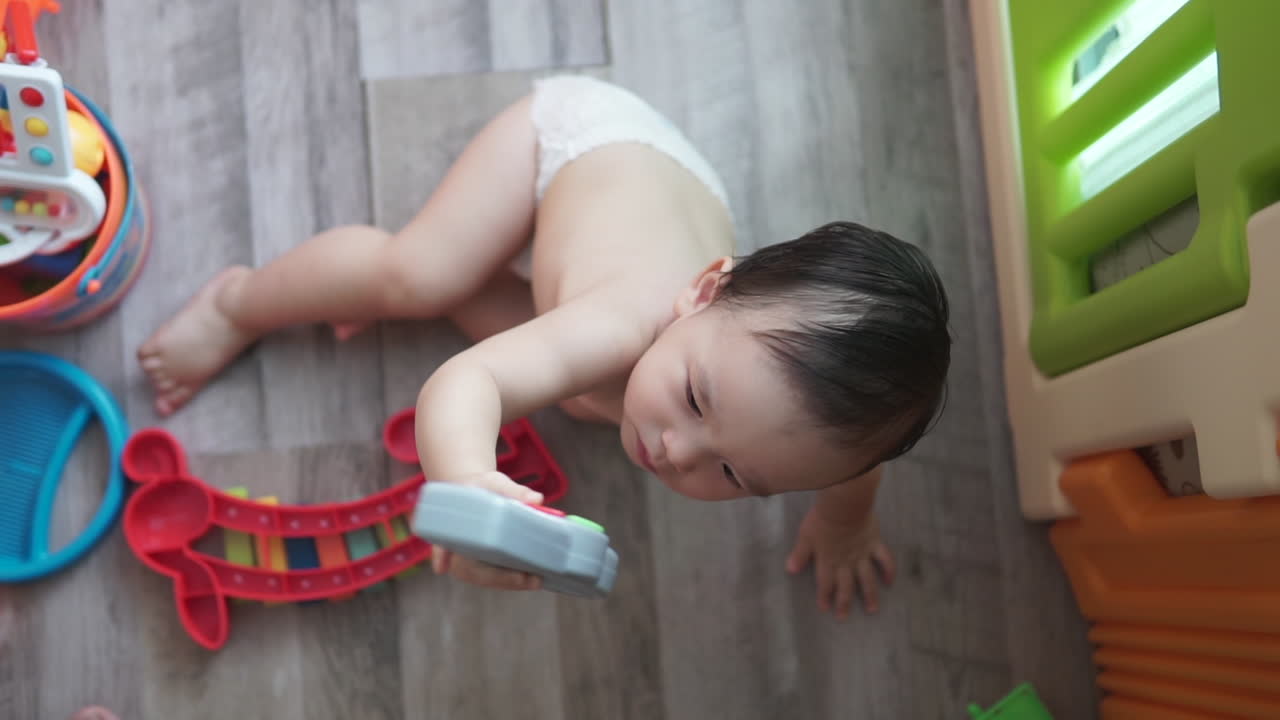 집에서 실내 플라스틱 놀이터에서 놀 수 있는 장난감을 제공하는 귀여운 1살 동아시아 소년의 슬로우 모션 하이 앵글 클립