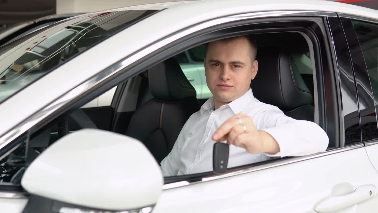 Happy stylish man showing keys of his new car in dealership. Auto business, car sale