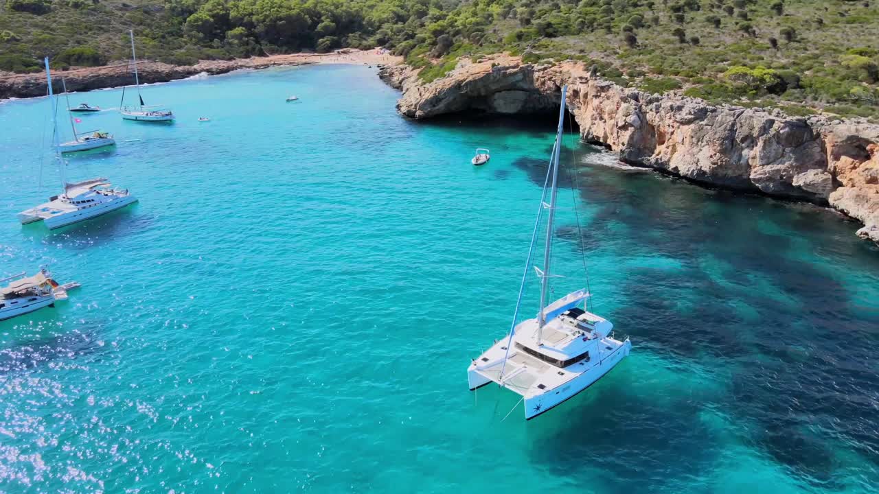 Experience the tranquil beauty of Cala Varques in Mallorca. Sailboats glide over crystal-clear turquoise waters surrounded by stunning cliffside landscapes. Perfect for boat lovers.