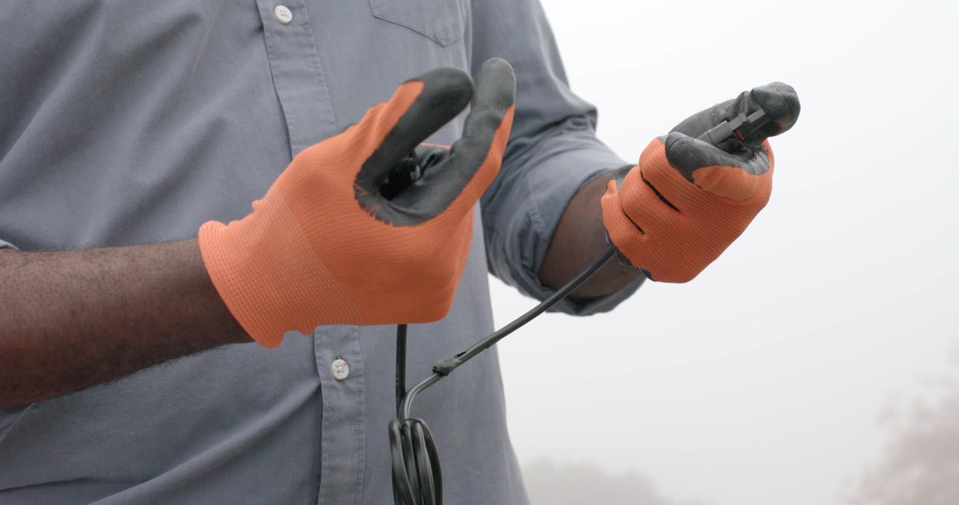 Voksen afrikansk mann med oransje hansker holder koblinger og inspiserer og viser en lås i tåke