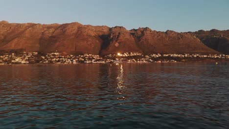 Eine-Wunderschöne-Aufnahme-über-Dem-Meer,-Die-Auf-Eine-Stadt-Mit-Einer-Bergkette-Dahinter-Zukommt