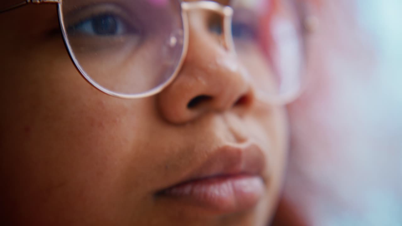 Young woman wearing glasses reading intently, focusing on text while moving eyes left to right, conveying deep concentration during study session