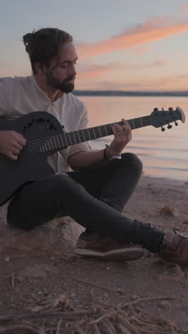 Man playing acoustic guitar by the lake at sunset