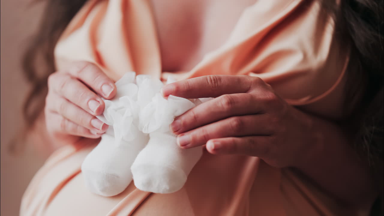 Primo piano di una donna incinta che tiene in mano e gioca con dei calzini bianchi da neonato sulla pancia