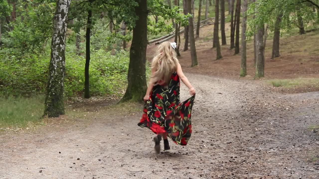 mujer joven atractiva con vestido largo corriendo por el bosque y mirando a su alrededor