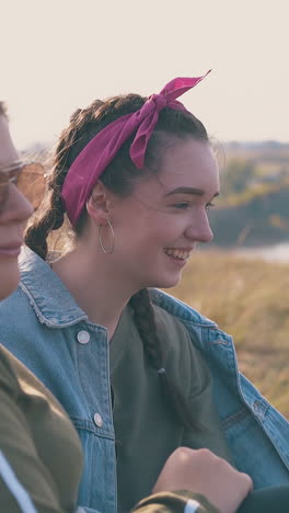 young overweight woman and girlfriend spend time on steep green river bank in warm autumn evening