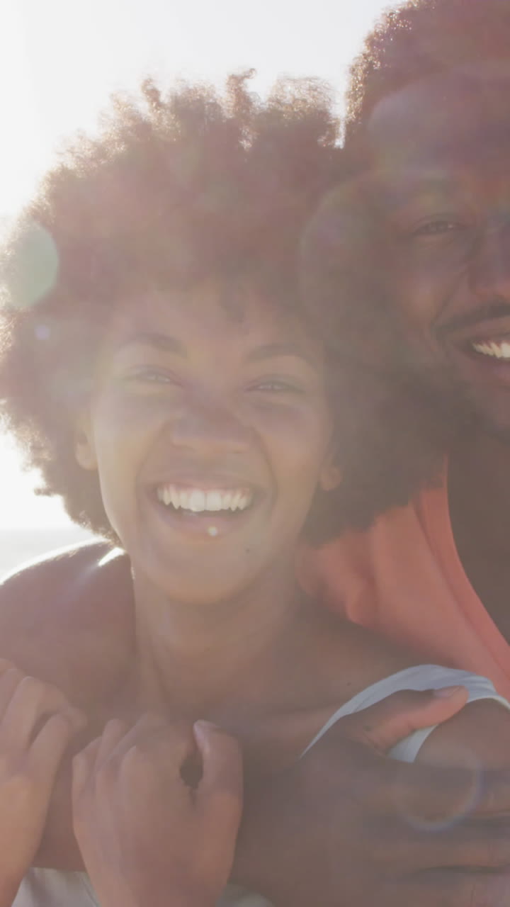 Portrait of smiling african american couple embracing on sunny beach