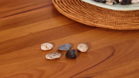 a hand arranges small stones on a wooden table in a well-lit room, creating a calm and focused atmosphere