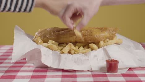 personas que usan los dedos para comer una comida tradicional británica de pescado y papas fritas
